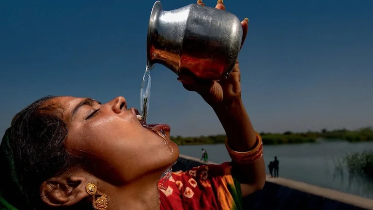 A woman drinking water outdoors beside a reservoir